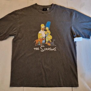 T-shirt "The Simpsons", mörkgrå H&M strl medium oversized - Mörkgrå t-shirt med tryck på framsidan "The Simpsons" från H&M, oanvänd. Tyget är inte vanligt t-shirt-tyg utan lite tjockare. Storleken är medium, oversized, så det är en STOR medium. 