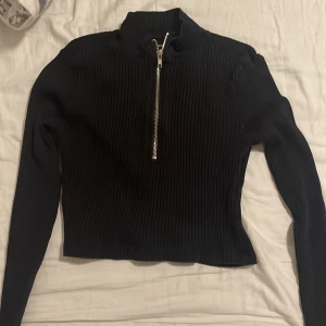 Svart tröja med guldig dragkedja - Svart tröja med dragkedja ganska långt upp på halsen, ärmarna är lite långa o är som en magtröja