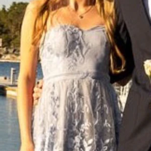 Balklänning från Lulus - Ljusblå balkänning med mjuk trikå inåt och fin spets-tyll utåt. Strl XS. Hon som använt den en gång är 167 cm lång, 50 kg, midja 64 cm och bystmått 78. https://www.lulus.com/products/andria-slate-blue-embroidered-strapless-maxi-dress/2046996.html