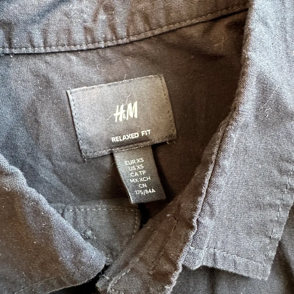 En svart kortärmad HM skjorta med storlek XS i passformen relaxed fit. En tunn skjorta som är perfekt i sommarvädret. Använts endast 2-3 gånger så funkar precis som ny. . Skjortor.