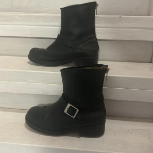 Johnny Bulls  - Johnny Bulls Low Boot Zip Back. Svarta med gulddetaljer. Använt skick. Gångveck på tårna. Sliten på sulan fram och bak. Äkta skinn. Strl 39 men passar även mig som vanligtvis har 40