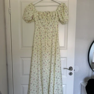 Gul lång blommmig klänning  - Säljer denna oanvända blommiga somriga långklänningen med puffärm och en slits i fram. Aldrig använd och säljer för 150kr. Strl xs