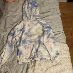 Blå och vit hoodie från Lindex - En blå och vit hoodie från Lindex i storlek 134/140 för barn. Hoodien har ett batikmönster och en fläck på framsidan. Den har långa ärmar och en huva.