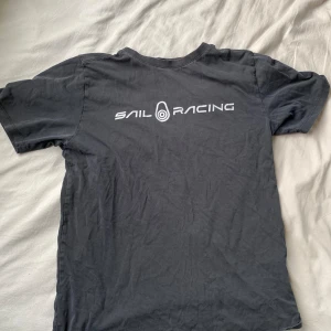 Svart t-shirt från Sail Racing - Säljer en svart t-shirt från Sail Racing. Den är i bra skick och har en cool logga på bröstetPerfekt för vardagsbruk eller träning. Passformen är normal. Skön och stilren t-shirt som passar till det mesta!