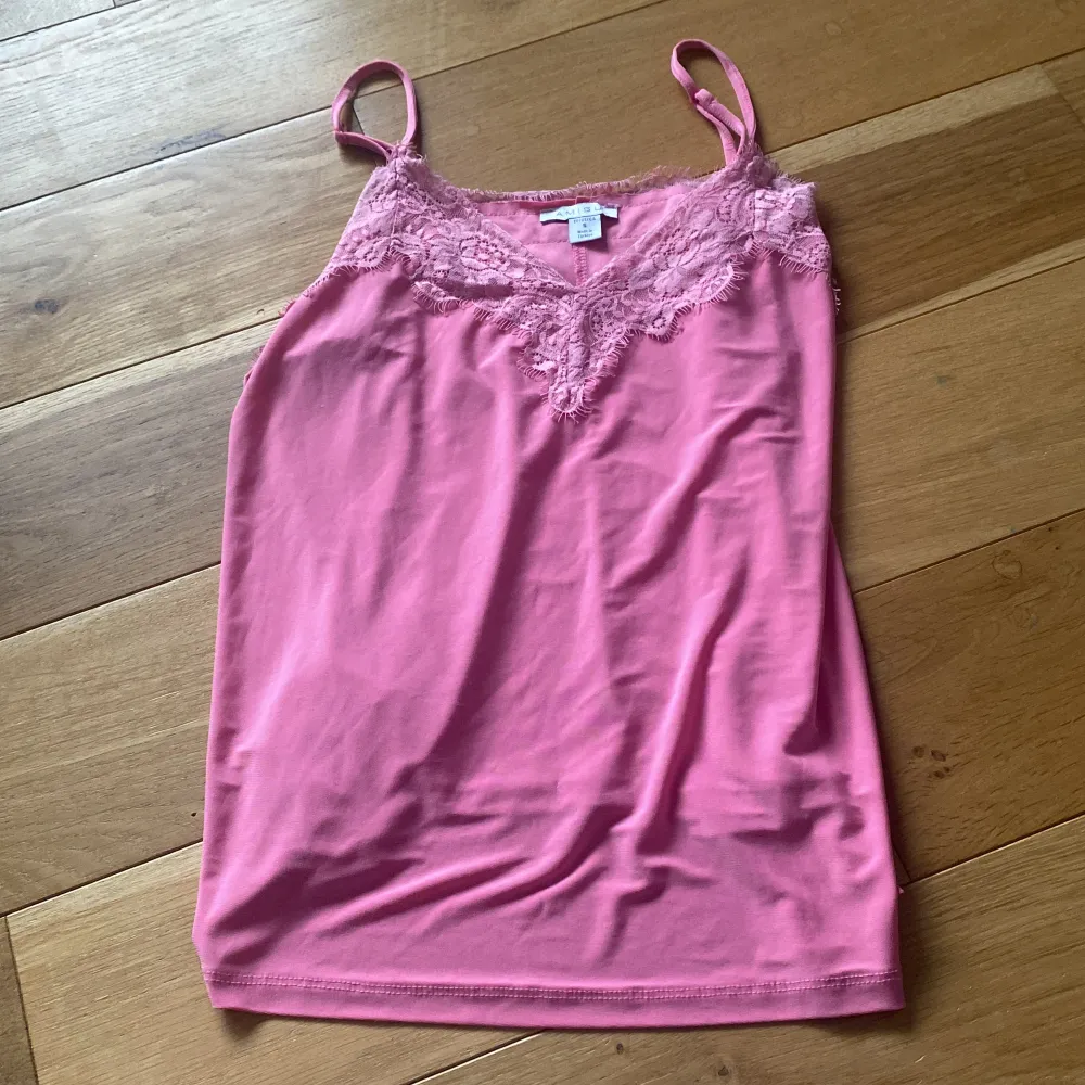 Säljer ett supergulligt rosa linne med spetsdetaljer runt halsringningen. Linnet har smala axelband och är perfekt för sommaren. Det är i bra skick och passar perfekt till både jeans och kjol. 🌸. Toppar.