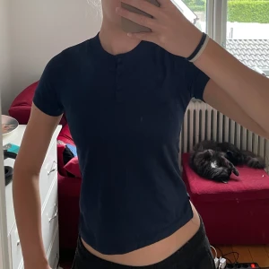 Mörkblå topp från JH Collection - Säljer en mörkblå topp från JH Collection. Den är kortärmad och har tre knappar vid halsen. Toppen är tight och tillverkad i ett mjukt och lätt material. Perfekt som tävlingströja till de flesta sporter.