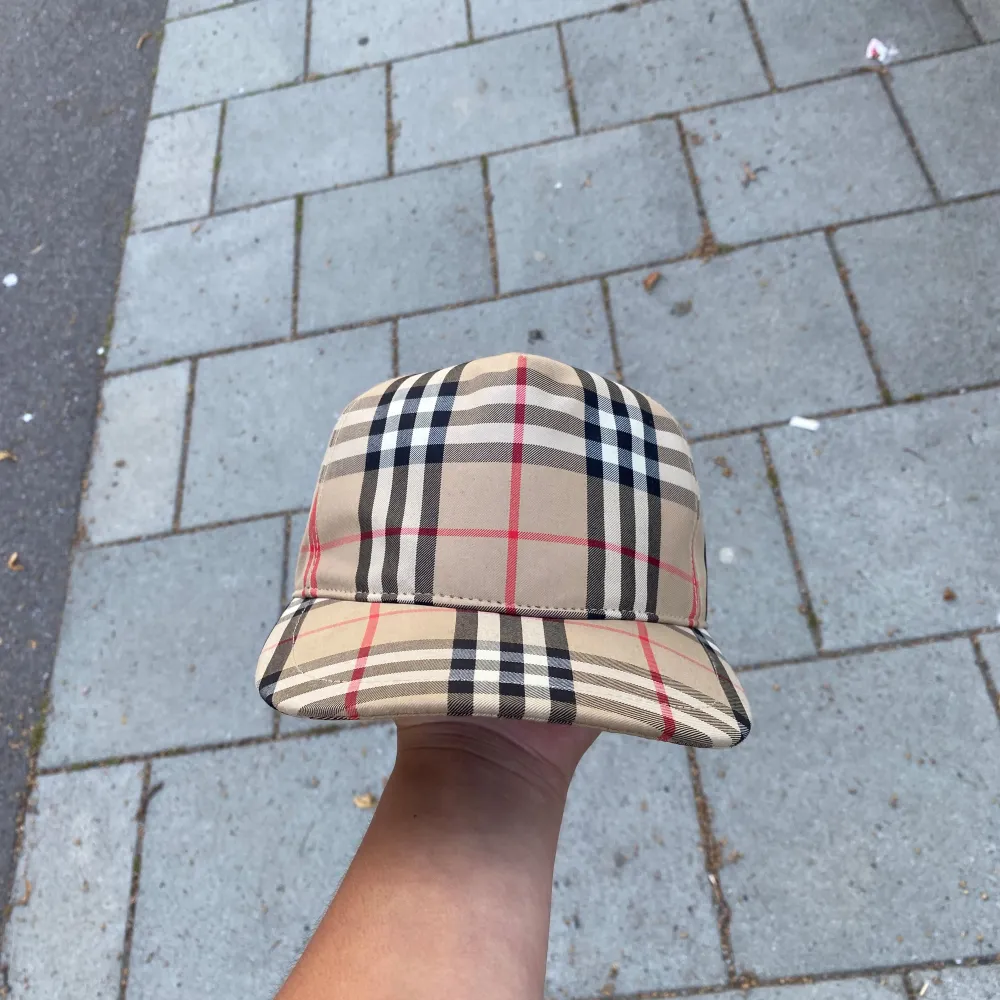 Säljer en snygg beige rutig keps från Burberry. Kepsen har det klassiska Burberry-mönstret i beige, svart och rött. Den är i nyskick och kommer med originalförpackning och påse. Perfekt för att ge din outfit en lyxig touch!. Övrigt.