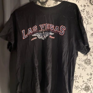 Svart Las Vegas t-shirt - Säljer en svart t-shirt med texten 'Las Vegas' i rött och vitt på framsidan. T-shirten är i bomull och har en normal passform. Perfekt för en casual look eller som souvenir från Las Vegas.