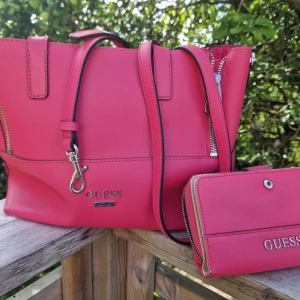 Guess väska med plånbok  - Guess väska i rosa färg med tillhörande plånbok. Den har lite slitage som syns på några av bilderna. Säljer båda tillsammans.