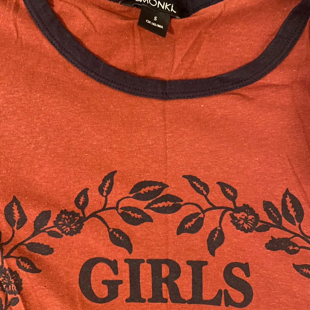 Säljer en snygg röd t-shirt från Monki med texten 'Girls Clique' i svart. T-shirten har korta ärmar och en rund halsringning med svarta detaljer. Perfekt för vardagsbruk eller en avslappnad dag ute. Den är i bra skick och väldigt bekväm att ha på sig. Passar perfekt till jeans eller shorts!. T-shirts.