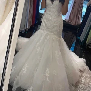 Vit spetsklänning med slits - Säljer en fantastisk vit klänning med spetsdetaljer och en elegant . Klänningen har en vacker låg rygg och är en brudklänning . Den är i nyskick och passar perfekt för din speciella dag. Klänningen är figursydd och har en vacker volangdetalj vid kjolen. Alla pärlor är handsydda. 