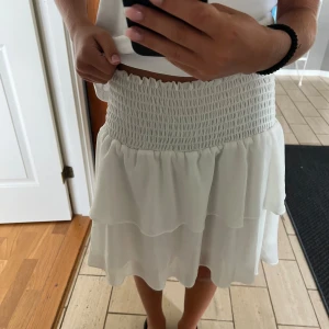 Vit kjol med volanger - Säljer en superfin vit kjol med volanger. Den har en elastisk midja. Perfekt för sommaren eller en fest! Kjolen är i nyskick och passar till många olika outfits. 🥰