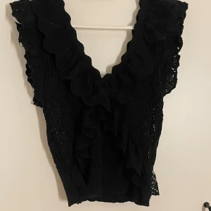 Svart stickad topp från Zara - Säljer en snygg svart stickad topp från Zara. Den har en vacker volangdetalj längs med halsringningen och är ärmlös. Helt oanvänd, köpt för 4 månader sedan. Perfekt för både vardag och fest! 🖤