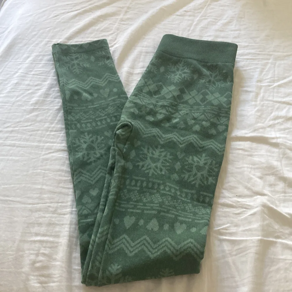 Ett par gröna leggings med ett vintermönster som inkluderar snöflingor och hjärtan. Tillverkade av 98% polyester och 2% elastan. Leggingsen har en mjuk insida för extra komfort.. Jeans & Byxor.