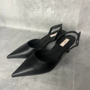 Pointy Low Heel NELLY - •klacksko från Nelly •spetsig tå •smal klack •justerbar rem runt hälen •klackhöjd 6cm •svart  •slutsåld online •använda en gång  •material: 40% polyester 60% reson •material insida: 40% polyester 60% reson •material yttersula: syntetiskt gummi