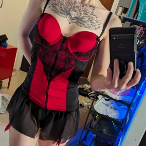 Hunkemöller nattlinne M - Svart/rött nattlinne underklänning ifrån Hunkemöller. Har bygel, dragkedja framtill samt strumpebandshållare Fint skick utom en liten fläck på ena kupan (se sista bilden, knappt synlig när den är pâ) vet ej om den går bort i tvätt