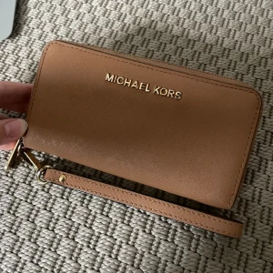 Michael Kors - Michael Kors plånbok i använt skick, därav priset. Rymmer mycket och är även fin som en clutch. Jag brukar ha mobilen där i med. 