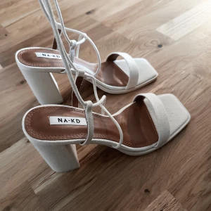 Beige klackskor från NA-KD storlek 38 - Beige klackskor som man knyter runt benen. Testade inomhus, aldrig använda. Helt nya! Storlek 38. 