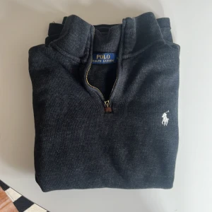 Ralph lauren quater zip ÄKTA - En elegant Ralph lauren Zip som är köpt på Plick innan. En äldre modell men är fortfarande i mycket bra skick och kvaliten är fantastisk. Dragkedjan fungerar men saknar en läder bit (bild 1). Utöver det är det inga defekter på tröjan. Kom med bud😁👍