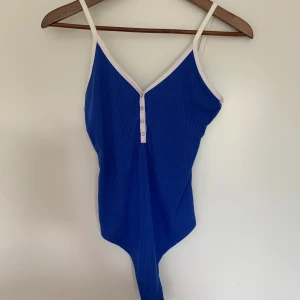 Blå bodysuit från BikBok - Blå bodysuit med vita detaljer från BikBok. Storlek XS. Oanvänd. Knäppning i grenen.