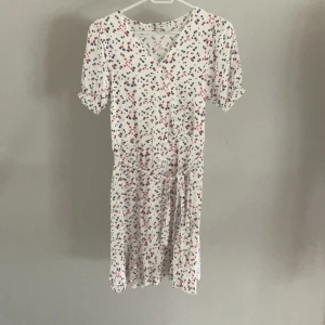 Omlottklänning - Jättefin omlottklänning som passar perfekt till sommaren. Mönstret med röda, gröna och blå blommor med vit botten.