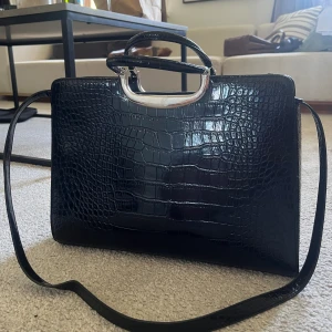 Svart väska - Svart väska/portfölj köpt secondhand med avtagbart längre axelband   Bredd: 37 cm  Djup: 9 cm Höjd: 26 cm 