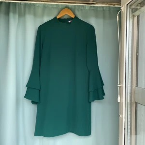 Klänning  - Långärmad grön klänning i gott skick ärmar med volang. Använd ett par gånger  98% Polyester  2% Elastisk 