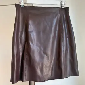 Mörkbrun kjol i läderimitation, Lindex  (Sista bilden visar kjolen i svart)  PU material yttre, polyester 96, elastane 4% linningen   Så snygg, men säljer pga för stor tyvärr.  Skick: använt skick men fräsch, inga skavanker