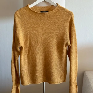 Stickad tröja - Stickad tröja i en snygg gul färg blandat med vit. Snygg detalj i armen, sitter åt runt handleden och går över handen. 
