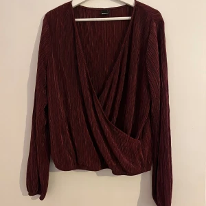 Vinröd blus - Härlig blus som aldrig behöver strykas, materialet ”blänker” vilket gör den väldigt snygg att ha på kvällen för en utgång eller roligare tillställning. En säkerhetsnål kan vara bra i urringningen vid mindre bröst, jag behövde dock inte det.