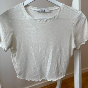 Skir topp/t-shirt i croppad modell. ”Volang” vid ärmslut och längst ner. Strechigt material. NA-KD. Storlek S. 100% polyester