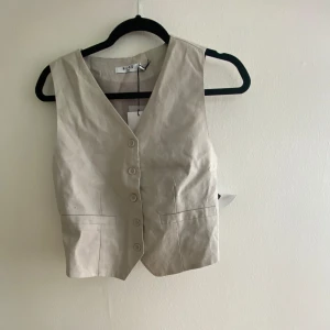 Beige väst  - Jättefin beige väst från NA-KD. Går att justera lite på spännet i ryggen. Helt oanvänd med lappen kvar!