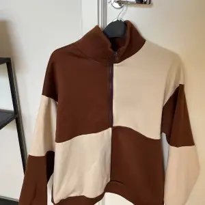Oversized sweatshirt med hög krage samt rutor med beige och brun färg. 