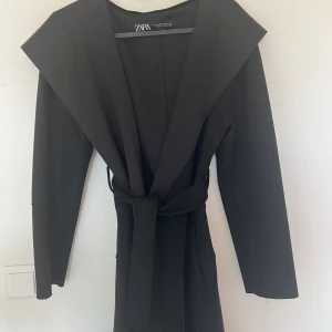 En svart vår/sommar kappa från Zara - Detta är en svart tunn kappa som funkar för både sommaren och våren. Som ni see på bilden är det väldigt skönt material. Den är i storlek S. Jag är 170 cm och den passar precis över knäna. 