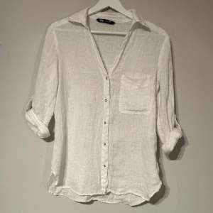 En vit linneskjorta från Zara i storlek XS. Skjortan har guldfärgade knappar, en ficka framtill och knappar på ärmarna så de både kan rullas upp eller inte. Skjortan har knappt använts och är i ett mycket bra skick.