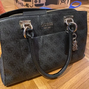 Guess handväska - Handväska från guess köpt i Åhléns. Bra/använt skick. Slitage under handtagen, inget som syns tydligt.  Hämtas i Kortedala. 