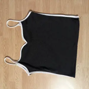 Snygg svart topp med band och vita detaljer runt formen på tröjan. Oanvänd, testad endast.