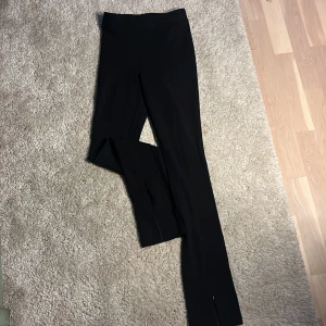 Svarta byxor med slits - Svarta byxor med dragkedja längs ner vid fötterna som går att reglera.