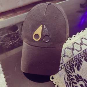 Mooseknuckles keps - En storlek passar unisex. Färgförändringar.  Från baksidan vid stängning finns ett litet bråck som inte påverkar det