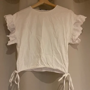 Vit t-shirt - Vit t-shirt med volang i ärmarna och knyten nere vid tröjan som man kan justera midjan (se bild). Strl S