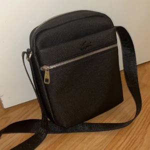 Lacoste väska - Väskan är bra har bara använt den några gånger men den är fortfarande som en ny väska. Väskan har inga skador eller nått sånt