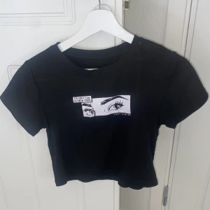 Svart Topp - Säljer min svarta croptop med tryck från brandy melville. något sprucket tryck, använd fåtal gånger.
