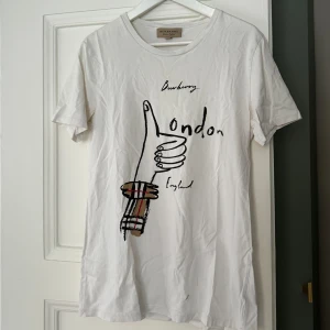 Burberry tshirt  - Vit burberry tshirt köpt på nk i Göteborg.  Storlek M.  Se sista bild med hål (föreslagna priset är därav nedsatt)   Meddela för fler bilder!  Mitt pris: 750kr. 