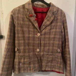 Billabong Kavaj - En rutig jacka/kavaj från Billabong. Färg: rutigt (beige/röd/svart), lila detaljer, rött innertyg. Storleken är lite oklar, står size 3 i innertyget, men passar som en s! Kavajen har en vit färgfläck på ena armen, dm för bild! 