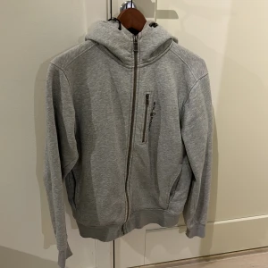 Sailracing hoodie -  En grå Sail racing hoodie, har små defekter på änden av armarna men märks knappt, prutbar