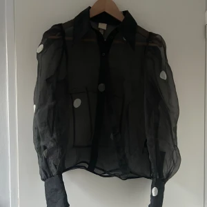 Skjorta i med vita prickar - Denna skjorta är i genomskinligt material och är figursydd i ryggen med puffärmar.  Den är använd fåtal gången och super snygg med ett linne eller bara bh under🖤🤍