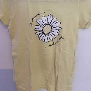 Ljus gul somrig tröja, den har en vit blomma i mitten med en liten text som de står ”Forever and a day” 