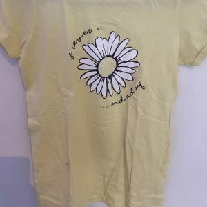 Tjej t-shirt  - Ljus gul somrig tröja, den har en vit blomma i mitten med en liten text som de står ”Forever and a day” 