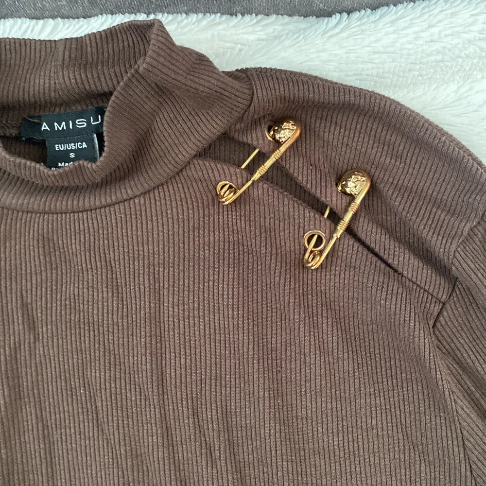 Fin ribbad brun tröja med kort hals och fin detalj vid vänster axel med fake säkerhetsnålar med detaljer i guld. Ej använd.. Tröjor & Koftor.