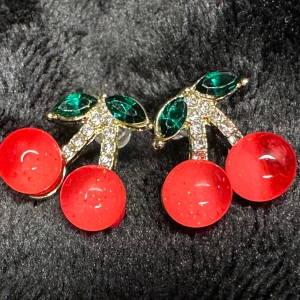 Nya örhängen m körsbär Retro Cirkon Kristall Cherries Cherry Kawai Rockabilly 50-tal 1950 Rock Pinup  - Så söta örhängen med körsbär och blad med glittrande zirkoner.  0,6x0,5 cm.  Stift - för dig som har hål i öronen. Med cubic zirkonia, kristall, akryl.  Nya och oanvända.  Jag skickar sålda varor en eller två gånger i veckan. 